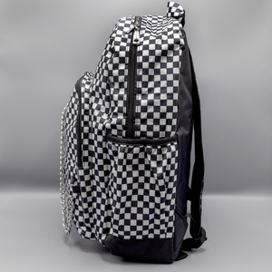 The White Checkerboard Backpack sat on a grey background. The vegan friendly bag features an all over mini black and white check print with black trim along the silver zips. The bag is facing left to highlight the two front zip pockets, two side elasticated pockets, the top zip compartment, the top handle and the silver decorative detachable chain draping across the front.